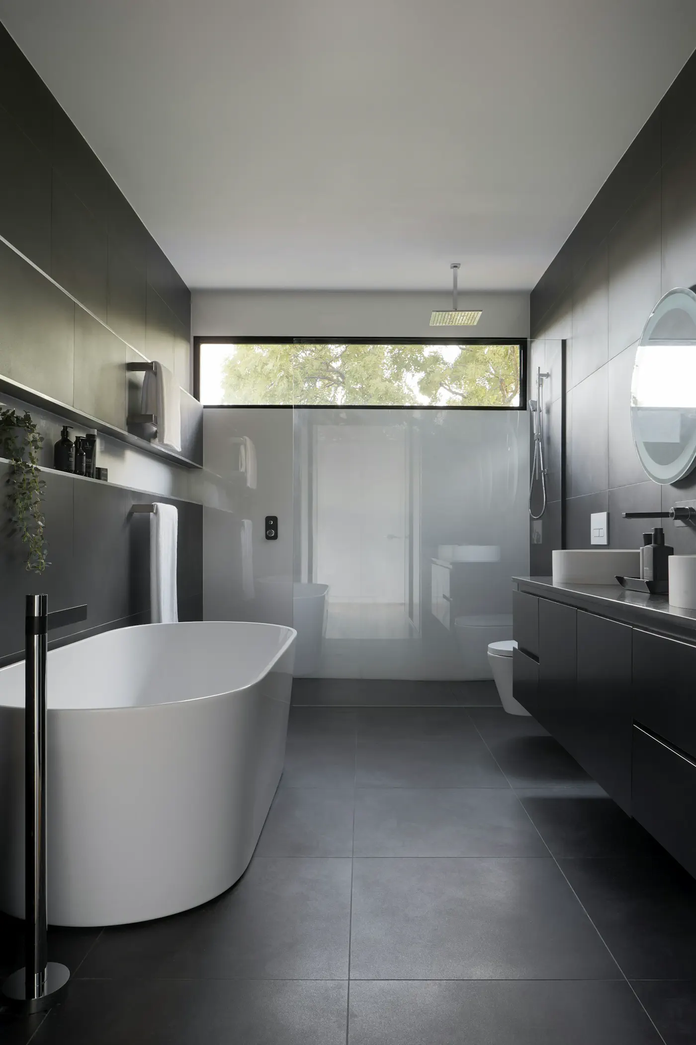 Dark-stone hotel bathroom with a freestanding tub, dual vanity, and walk-in shower — editorial still